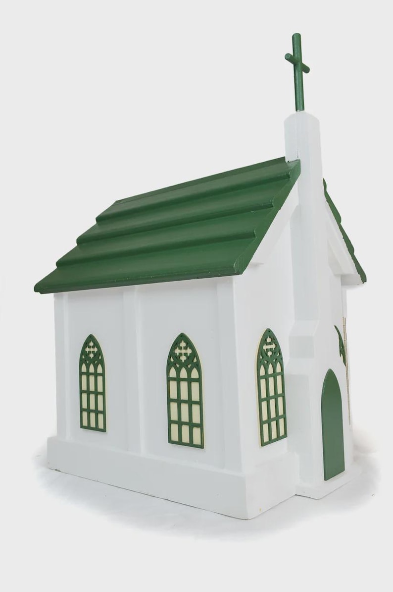 May include: A white miniature church with a green roof and cross. The building has three arched windows with green trim and a green door. The church is a decorative item.