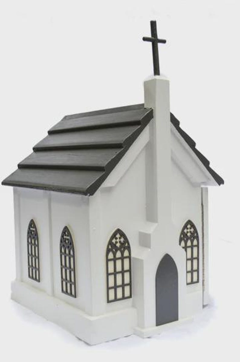 May include: A white miniature church with a black roof and cross. The church features arched windows with decorative black frames and a dark gray door. The overall design is a simple, yet elegant, representation of a church.