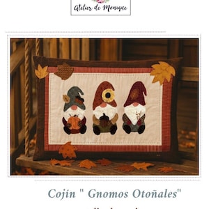 Puede incluir: Un cojín rectangular con tres figuras de gnomos con detalles otoñales. Los gnomos tienen sombreros puntiagudos y sostienen calabazas y bellotas. El cojín está enmarcado con un borde marrón y adornado con aplicaciones de hojas. El texto "Atelier de Monique" está arriba.