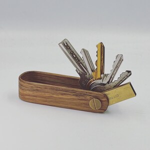 Op de afbeelding: Een houten sleutelhanger met een messing schroef en een set sleutels. De hanger is gemaakt van lichtbruin hout met een nerfpatroon. De sleutels zijn zilver en goud.