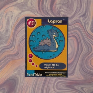 May include: A Pokémon trading card featuring Lapras, a blue and gray sea creature. The card has a blue and yellow design with the number 131. Text on the card includes "Weight: 485 lbs. Height: 8'2" and "PokéTrivia."
