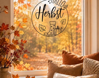 Könnte beinhalten: Eine gemütliche Herbstszene mit einem Fenster, das eine runde Grafik mit der Aufschrift "Hallo Herbst" zeigt. Das Fenster ist von Herbstlaub umgeben. Kissen, Kürbisse und eine brennende Kerze schaffen eine warme, einladende Atmosphäre.