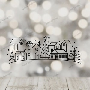 May include: A black and white line drawing of a village scene with houses, trees, and a star on top of a Christmas tree. The background is a blurred bokeh effect with a wooden surface in the foreground.