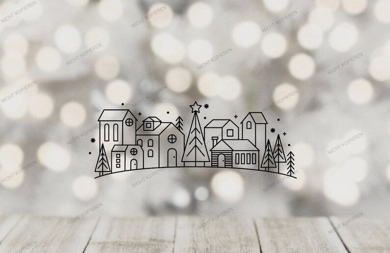 May include: A black and white line drawing of a village scene with houses, trees, and a star on top of a Christmas tree. The background is a blurred bokeh effect with a wooden surface in the foreground.