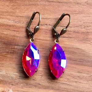 May include: A pair of dangle earrings with a marquise-shaped iridescent red crystal and a gold-toned hook closure.