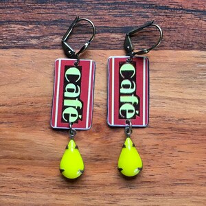 May include: A pair of dangle earrings with a red and white rectangular charm that says "café" in green letters. Each charm has a yellow teardrop-shaped pendant.