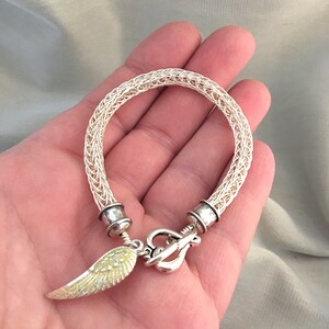 Op de afbeelding: Een zilveren draad armband met een zilveren sluiting en een gele engelenvleugel bedel.