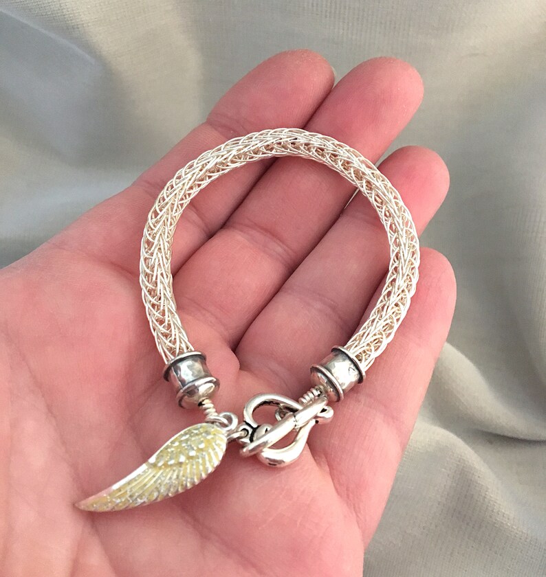 Op de afbeelding: Een zilveren draad armband met een zilveren sluiting en een gele engelenvleugel bedel.