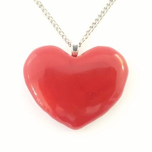 Puede incluir: Un collar con colgante de coraz&oacute;n rojo con una cadena plateada. El coraz&oacute;n es de color rojo brillante y liso. La cadena es una delicada cadena de eslabones plateada, adecuada para el uso diario.