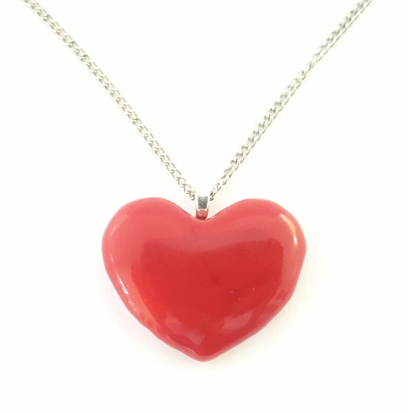 Puede incluir: Un collar con colgante de coraz&oacute;n rojo con una cadena plateada. El coraz&oacute;n es de color rojo brillante y liso. La cadena es una delicada cadena de eslabones plateada, adecuada para el uso diario.