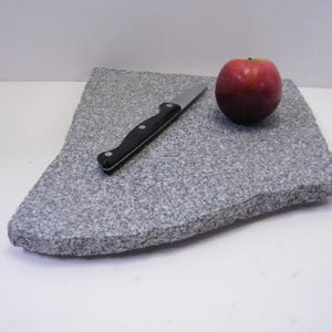 May include: A gray granite cutting board with a black-handled knife and a red apple. The cutting board has a rough, textured surface. The apple is a deep red color.