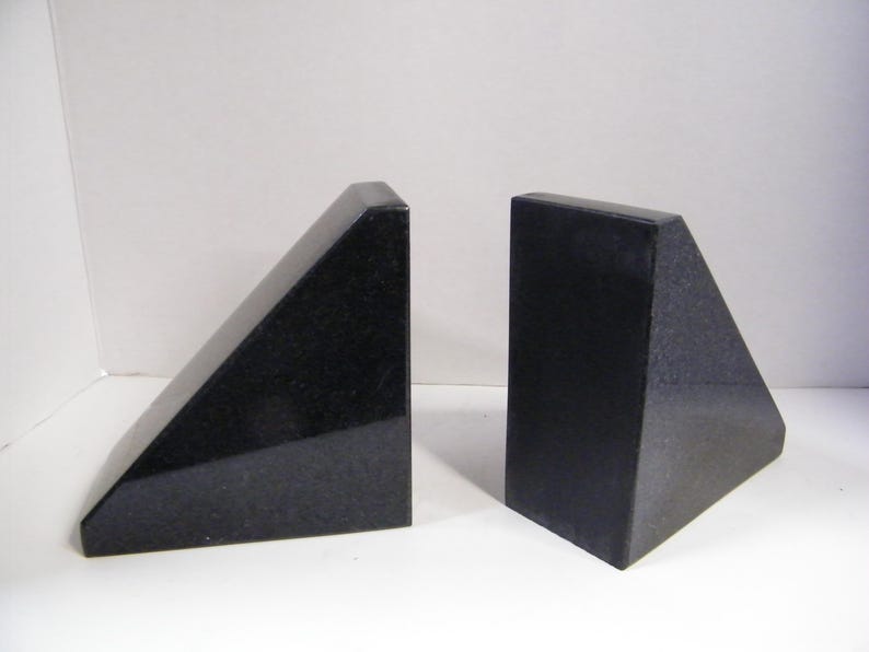 Puede incluir: Dos sujetalibros de granito negro. Cada sujetalibros tiene forma de tri&aacute;ngulo rect&aacute;ngulo con una parte superior plana y un acabado pulido. Los sujetalibros se muestran sobre una superficie blanca.