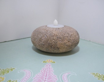 May include: A round, light brown stone candle holder with a white LED tea light inside. The candle holder is sitting on a light blue surface with a floral pattern.
