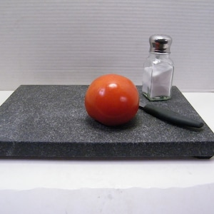 May include: A black granite cutting board with a red tomato, a small salt shaker, and a black knife.