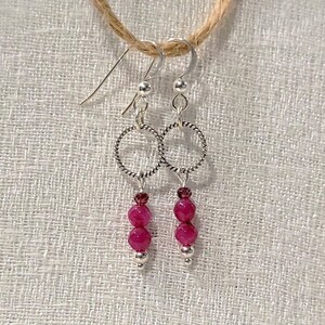 May include: A pair of silver earrings with a circle design and pink beads hanging from them.