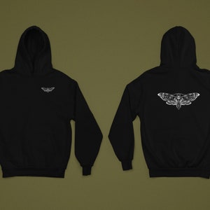 Puede incluir: Sudadera con capucha negra con un dise&ntilde;o de polilla blanca en la parte delantera y trasera. La parte delantera presenta un peque&ntilde;o gr&aacute;fico de polilla, mientras que la parte trasera muestra una polilla m&aacute;s grande con un dise&ntilde;o de calavera. La sudadera tiene capucha y mangas largas.