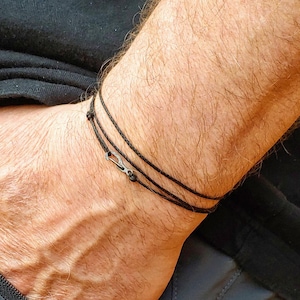 May include: A black cord bracelet with a small silver clasp. The bracelet is worn on a person's wrist.