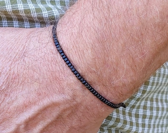 May include: A simple black beaded bracelet on a person's wrist.