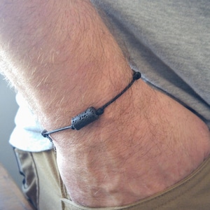 May include: A black bracelet with a small, dark grey lava rock bead.