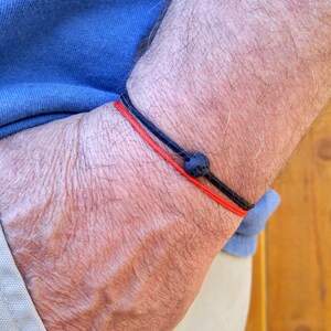 May include: A red and black bracelet with a black lava rock bead. The bracelet is worn on a person's wrist.