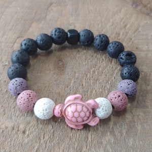 Op de afbeelding: Een armband van zwarte lavasteen met roze en witte kralen en een roze schildpadbedel.
