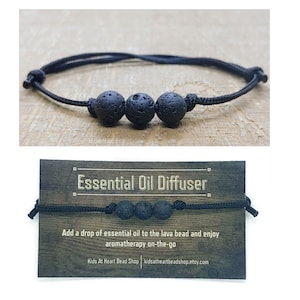 May include: Black lava bead bracelet with a black cord. The bracelet is an essential oil diffuser. The text on the card reads "Essential Oil Diffuser. Add a drop of essential oil to the lava bead and enjoy aromatherapy on-the-go. Kids At Heart Bead Shop kidsatheartbeadshop.etsy.com"
