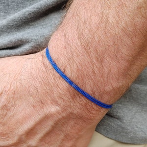 Peut inclure: Un bracelet en cordon tressé bleu sur le poignet d'une personne.