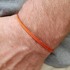 May include: A close-up of a person's wrist wearing a simple orange string bracelet.