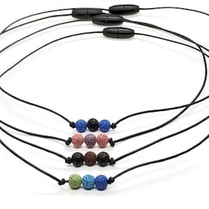 May include: Four black cord necklaces with adjustable magnetic clasps. Each necklace features a different set of lava rock beads in various colours, including blue, green, brown, and pink.
