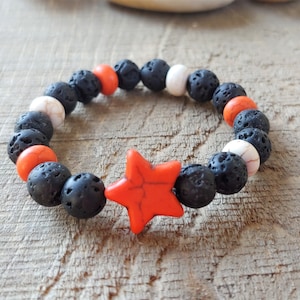 May include: A black lava rock bracelet with orange and white beads and a red star charm.