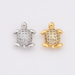 May include: Two turtle charms, one silver and one gold, both with clear crystal accents.