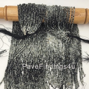 May include: A strand of gray and black gemstone beads, approximately 4mm in size, strung on black thread. The beads are faceted and have a shimmery, iridescent finish. The strand is displayed on a wooden dowel rod. The text "PaveFindings4u" is visible in the image.