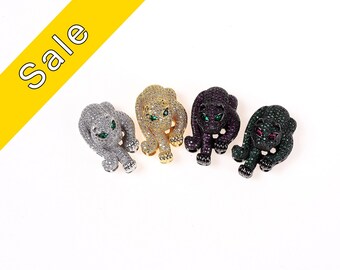 May include: Four panther charm pendants with green and red eyes. The charms are made of metal and are covered in clear, gold, purple, and green rhinestones.