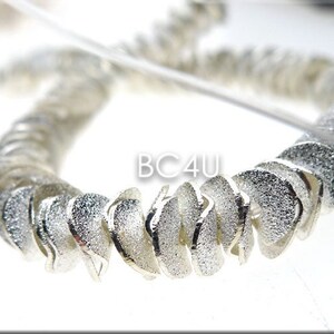 May include: A silver bracelet made of small, textured, crescent-shaped links. The bracelet is twisted and has a shiny finish.