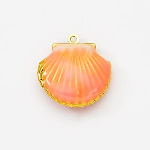 May include: A gold-tone seashell charm with a pink and white enamel finish. The charm is designed to look like a seashell with a detailed, textured surface.