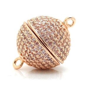 May include: Rose gold tone magnetic clasp with a round, sparkly design. The clasp is made of metal and has a polished finish.
