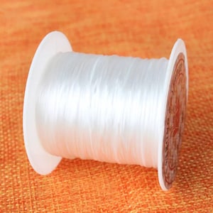 May include: A spool of white elastic cord for jewellery making. The cord is wound around a white plastic spool with a label that says "Elastic Cord".