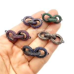Op de afbeelding: Vijf zwarte metalen connector charms met verschillende gekleurde kristal accenten. De charms zijn gevormd als twee in elkaar grijpende cirkels. De kleuren zijn groen, paars, roze, bruin en blauw.