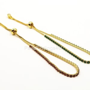 May include: Two gold chain bracelets with adjustable sliding clasps. One bracelet has green cubic zirconia stones and the other has red cubic zirconia stones.