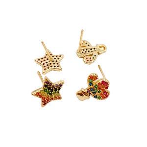 K&ouml;nnte beinhalten: Ein Set aus drei goldfarbenen Ohrringen mit bunten Kristall-Akzenten. Die Ohrringe haben ein Stern-, Schmetterlings- und Blumendesign.