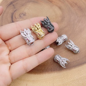 May include: Five silver dragon head charms with pink accents. The charms are in various positions on a wooden surface.