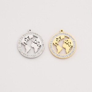 May include: Two round pendants featuring a world map design. One pendant is silver-colored, the other is gold-colored. Both pendants have a ring of clear crystals around the edge, adding sparkle. The world map is cut out, showing the continents.