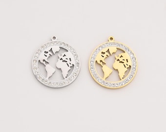 May include: Two round pendants featuring a world map design. One pendant is silver-colored, the other is gold-colored. Both pendants have a ring of clear crystals around the edge, adding sparkle. The world map is cut out, showing the continents.