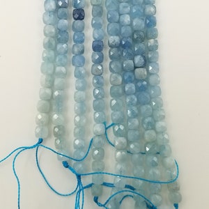 May include: Strands of aquamarine gemstone beads in varying shades of blue. The beads are square-cut and strung on blue thread. The color palette ranges from light, almost white-blue to deep, saturated blues. Ideal for jewelry making.
