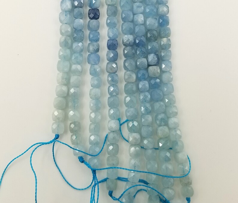 May include: Strands of aquamarine gemstone beads in varying shades of blue. The beads are square-cut and strung on blue thread. The color palette ranges from light, almost white-blue to deep, saturated blues. Ideal for jewelry making.
