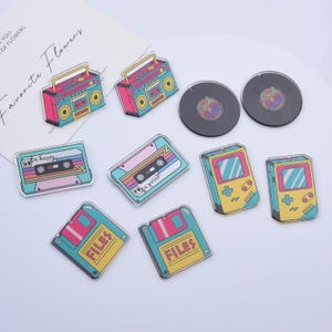 May include: A set of nine colorful retro-themed acrylic charms featuring a cassette tape, a boombox, a floppy disk, a video game console, and a record. The charms are perfect for adding a touch of nostalgia to your keychain, bag, or jewelry.