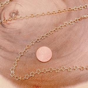 Puede incluir: Collar de cadena de estrellas doradas sobre una superficie de madera. La cadena es del tamaño de una moneda de un centavo de euro.
