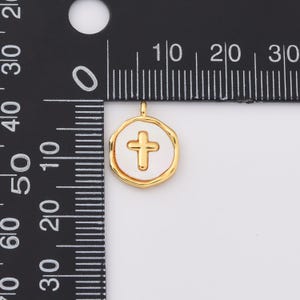 Op de afbeelding: Gouden hanger met een witte emaille cirkel met een gouden kruis in het midden. De hanger is ongeveer 1 cm in diameter.