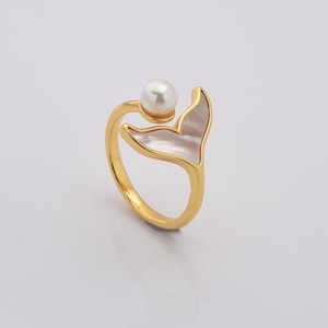 May include: Gold ring featuring a white pearl and a white shell mermaid tail design.