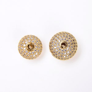 May include: Two gold-toned round beads with a hole in the center. The beads are covered in small, clear rhinestones.